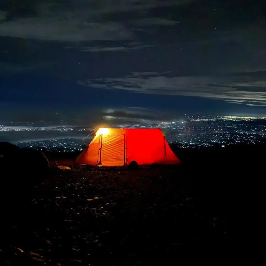 Night view of a high-altitude tent at Barafu Camp on Mount Kilimanjaro, with clear skies and the silhouette of the summit in the background