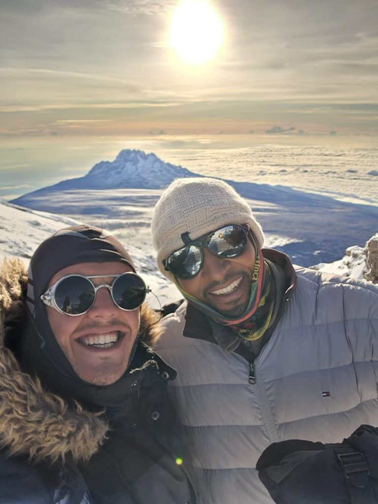 Two climbers on the snowy slopes of Mount Kilimanjaro, warmly dressed and illuminated by sunlight during a guided trek on the Northern Circuit Route with Kilimanjaro Joy