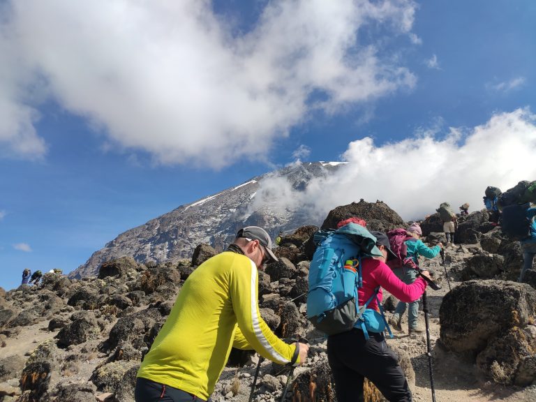 A group of climbers walking in single file on the rocky section of Kilimanjaro, part of a Kilimanjaro Joy Travel trek.