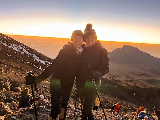 Two female hikers smiling on Mount Kilimanjaro with a warm sunset in the background during a guided trek
