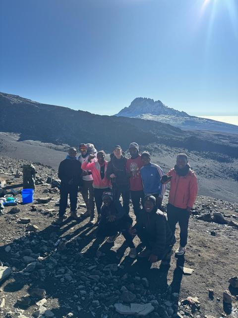 A group of hikers standing on Mount Kilimanjaro with the summit behind them and the sun shining in the background